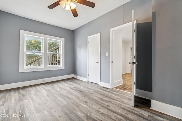 unfurnished bedroom featuring ceiling fan, a textured ceiling, baseboards, and wood finished floors