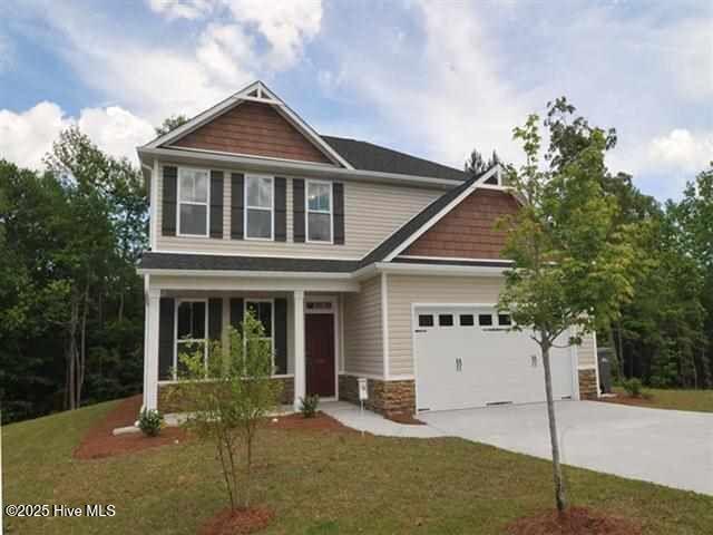 craftsman-style home featuring a garage, stone siding, a front lawn, and concrete driveway