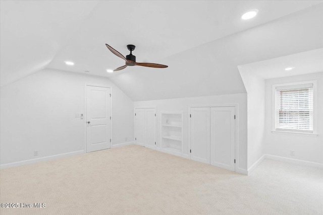 additional living space with built in shelves, ceiling fan, lofted ceiling, and light carpet