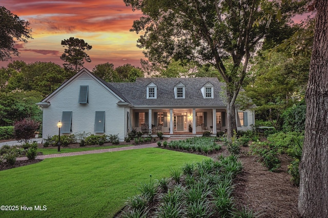 cape cod house featuring a yard and covered porch