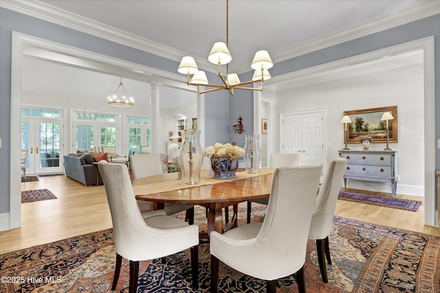 dining room featuring ornate columns, crown molding, an inviting chandelier, and light hardwood / wood-style flooring