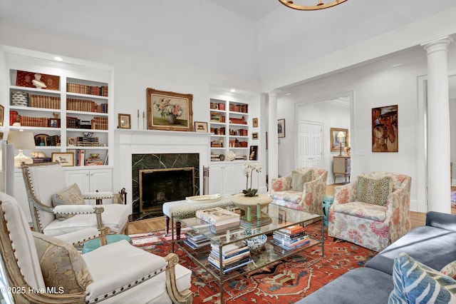 living room with ornate columns, a premium fireplace, hardwood / wood-style floors, and built in shelves