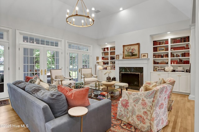 living room featuring light wood-type flooring, built in features, a high end fireplace, and french doors