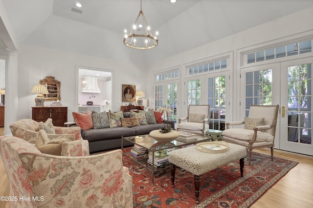 living room with high vaulted ceiling, a notable chandelier, light wood-type flooring, and french doors