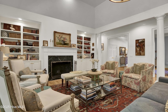 living room featuring hardwood / wood-style flooring, a high ceiling, a high end fireplace, built in shelves, and ornate columns