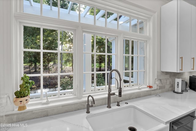 kitchen with plenty of natural light, sink, dishwashing machine, white cabinets, and light stone countertops