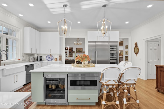 kitchen featuring hanging light fixtures, appliances with stainless steel finishes, a kitchen island, beverage cooler, and white cabinets