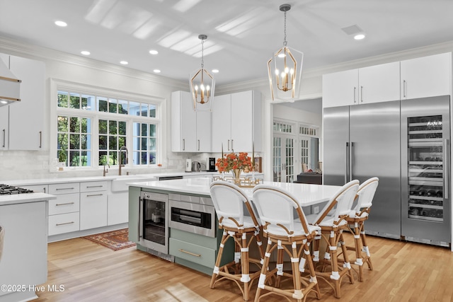 kitchen with pendant lighting, sink, built in refrigerator, white cabinetry, and a center island