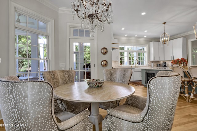 dining room featuring sink, wine cooler, a notable chandelier, crown molding, and light hardwood / wood-style flooring