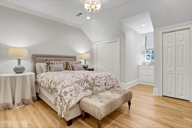 bedroom with hardwood / wood-style floors, two closets, lofted ceiling, ornamental molding, and an inviting chandelier