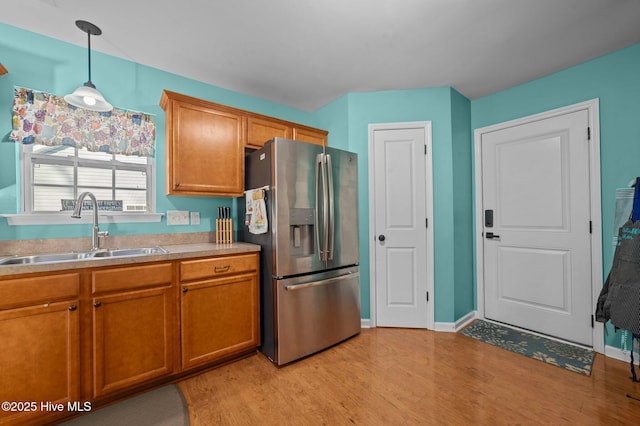 kitchen with stainless steel fridge with ice dispenser, hanging light fixtures, sink, and light wood-type flooring