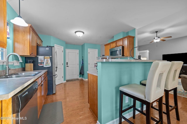 kitchen featuring decorative light fixtures, sink, kitchen peninsula, stainless steel appliances, and light hardwood / wood-style flooring