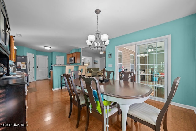 dining room with ceiling fan with notable chandelier and light hardwood / wood-style floors