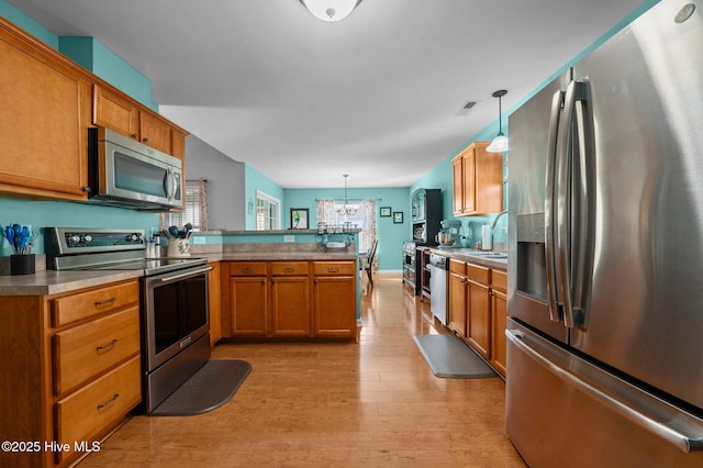 kitchen featuring appliances with stainless steel finishes, a healthy amount of sunlight, kitchen peninsula, and decorative light fixtures