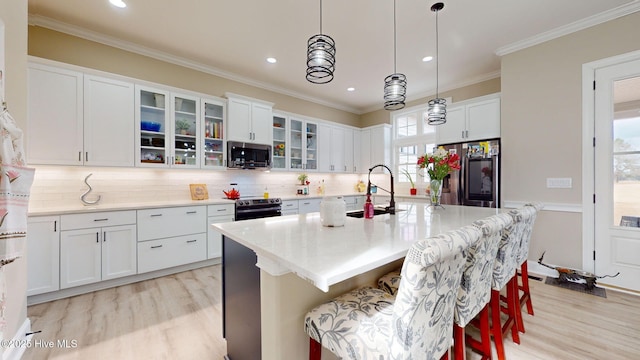 kitchen featuring white cabinetry, appliances with stainless steel finishes, an island with sink, and decorative light fixtures