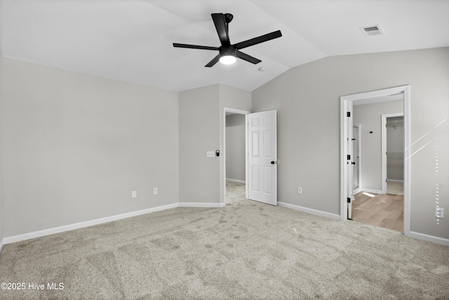 unfurnished bedroom featuring vaulted ceiling, ceiling fan, a spacious closet, and light colored carpet