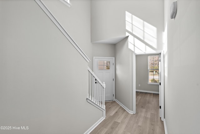 hall with light wood-type flooring and a towering ceiling