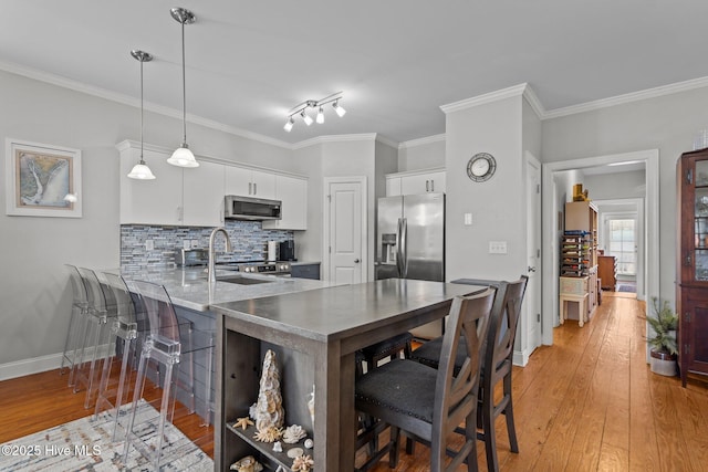 kitchen featuring white cabinetry, hanging light fixtures, light wood-type flooring, kitchen peninsula, and stainless steel appliances