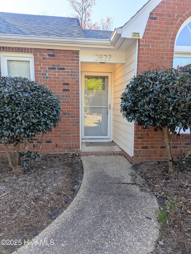 property entrance featuring brick siding and roof with shingles