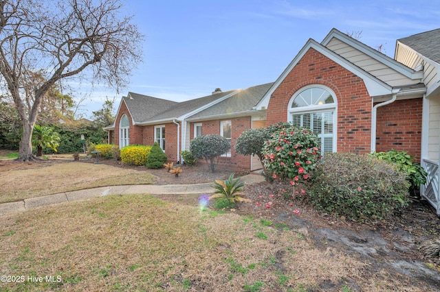 view of front facade featuring a chimney, brick siding, roof with shingles, and a front yard