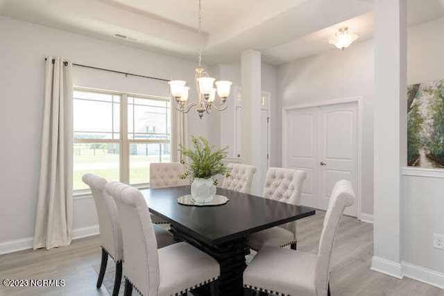 dining room featuring a chandelier, light hardwood / wood-style floors, and a raised ceiling