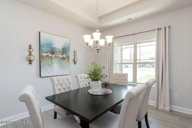 dining room with a notable chandelier, a tray ceiling, and wood-type flooring