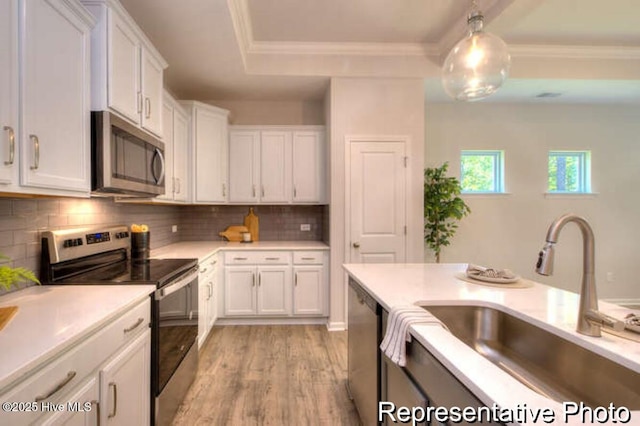 kitchen with sink, light hardwood / wood-style flooring, stainless steel appliances, white cabinets, and decorative light fixtures