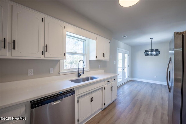 kitchen with sink, appliances with stainless steel finishes, white cabinets, decorative light fixtures, and light wood-type flooring