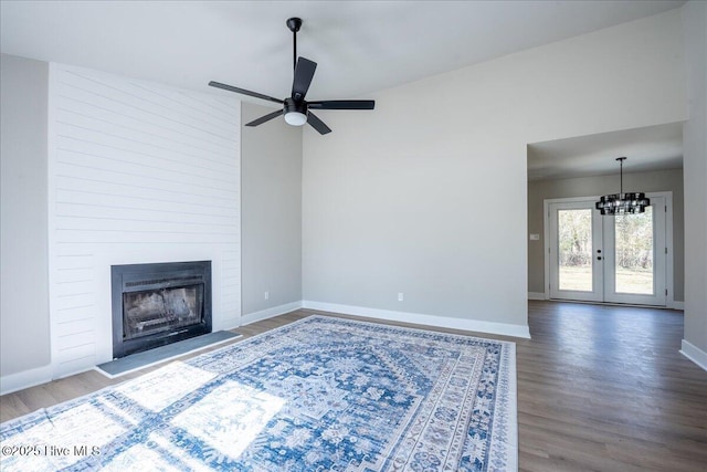 unfurnished living room featuring hardwood / wood-style flooring, a large fireplace, ceiling fan with notable chandelier, and french doors