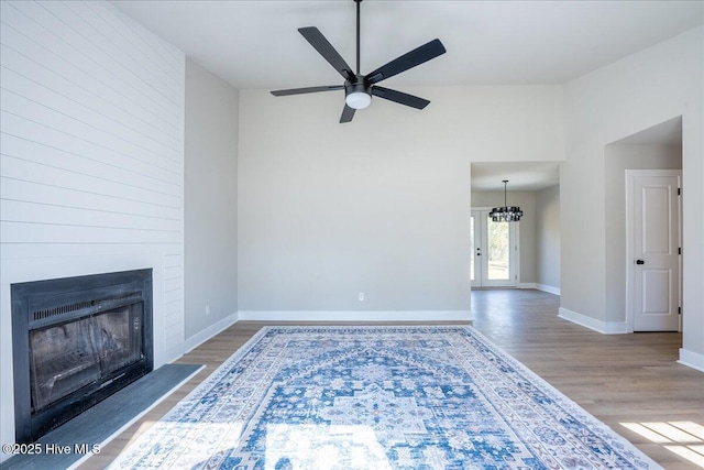 unfurnished living room with wood-type flooring, a fireplace, and ceiling fan with notable chandelier