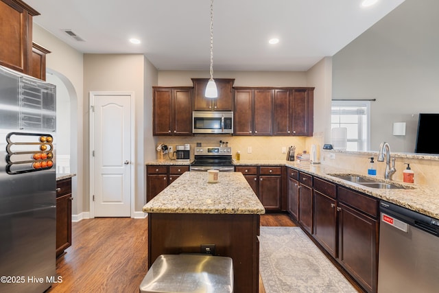 kitchen featuring sink, light stone counters, appliances with stainless steel finishes, a kitchen island, and pendant lighting