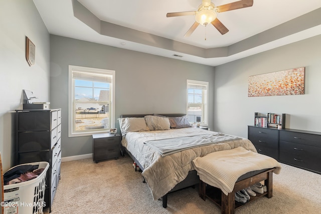 bedroom featuring ceiling fan, light colored carpet, and a raised ceiling