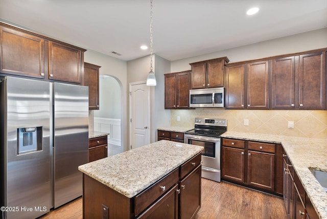kitchen with light stone counters, visible vents, appliances with stainless steel finishes, arched walkways, and wood finished floors