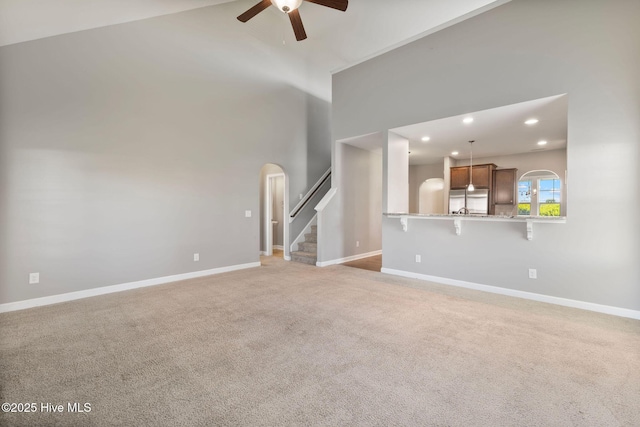 unfurnished living room with light carpet, a high ceiling, a ceiling fan, stairs, and arched walkways