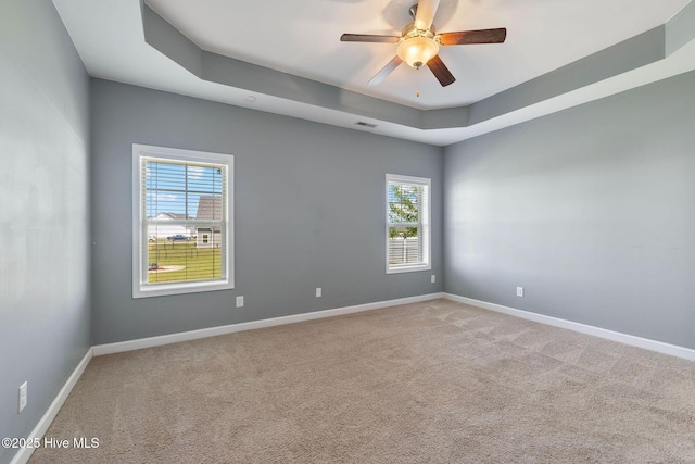 carpeted spare room featuring ceiling fan, a raised ceiling, and baseboards