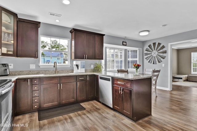 kitchen with sink, appliances with stainless steel finishes, light stone countertops, kitchen peninsula, and light wood-type flooring