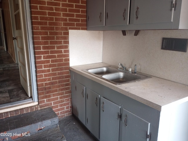 kitchen featuring gray cabinets, brick wall, and sink