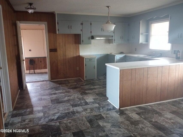 kitchen featuring pendant lighting, sink, wooden walls, and kitchen peninsula