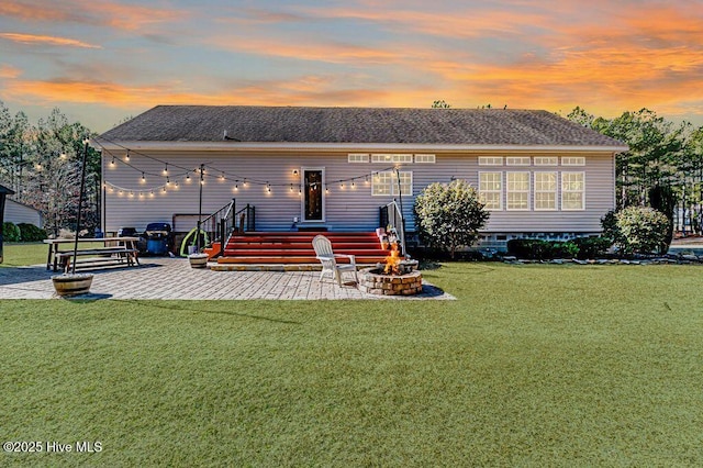 back house at dusk with a patio, a yard, and a fire pit