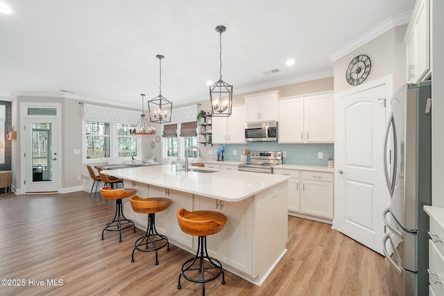 kitchen featuring sink, white cabinetry, decorative light fixtures, a center island with sink, and stainless steel appliances