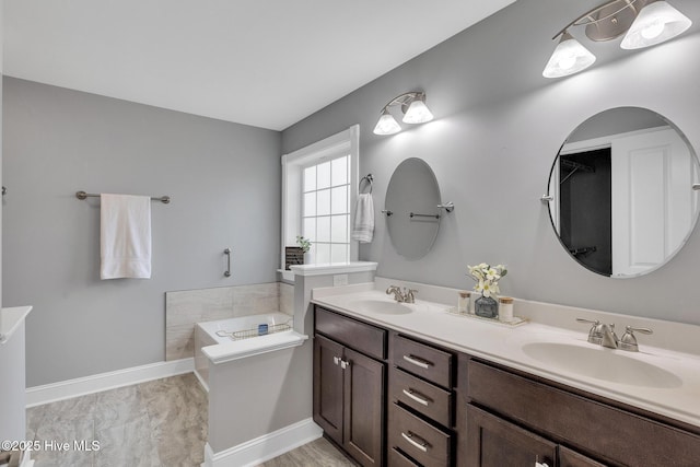 bathroom with a garden tub, double vanity, and baseboards