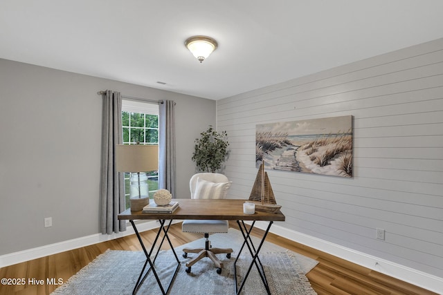 office area featuring baseboards, wood finished floors, and wood walls