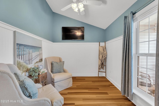 living area featuring vaulted ceiling, wood finished floors, wainscoting, and a ceiling fan