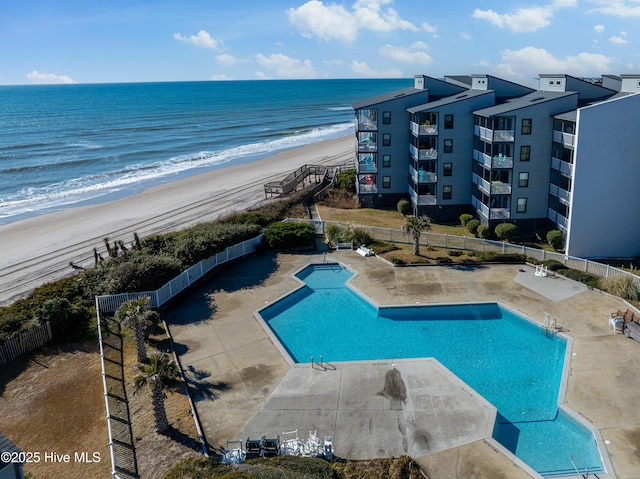 view of swimming pool featuring a water view, a patio area, and a view of the beach