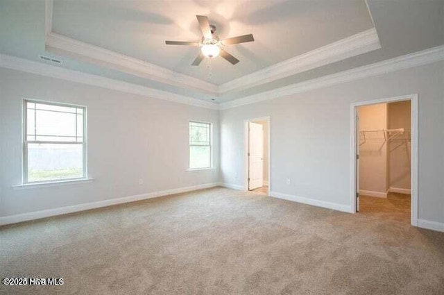 unfurnished bedroom featuring ornamental molding, a walk in closet, light colored carpet, and a tray ceiling