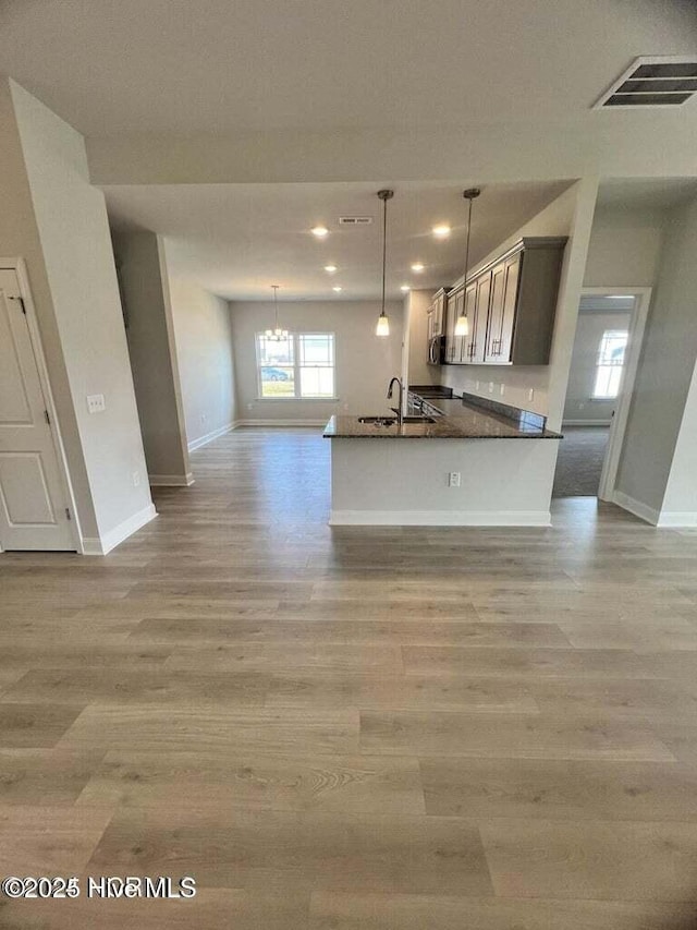 kitchen with sink, decorative light fixtures, kitchen peninsula, a notable chandelier, and light hardwood / wood-style floors