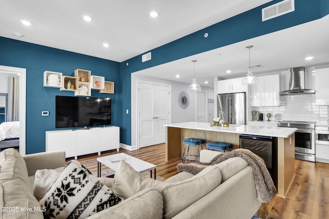 living area with wine cooler, visible vents, recessed lighting, and wood finished floors