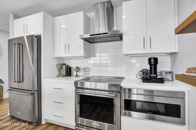 kitchen featuring decorative backsplash, stainless steel appliances, light countertops, wall chimney range hood, and white cabinetry