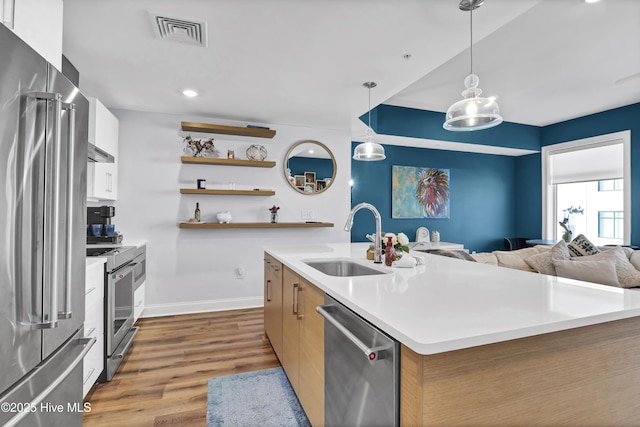 kitchen with stainless steel appliances, wood finished floors, a sink, visible vents, and open floor plan