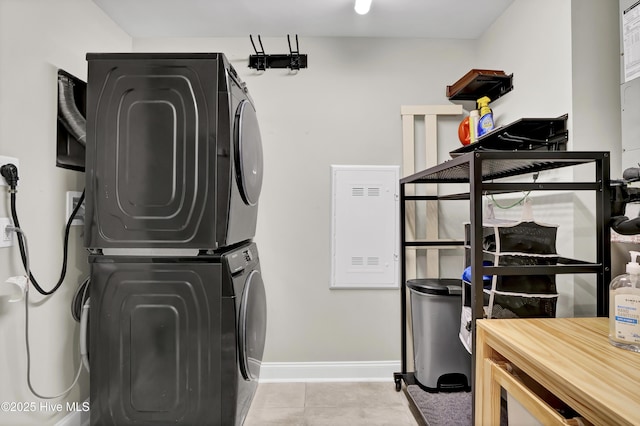 clothes washing area with laundry area, light tile patterned floors, baseboards, and stacked washer / drying machine